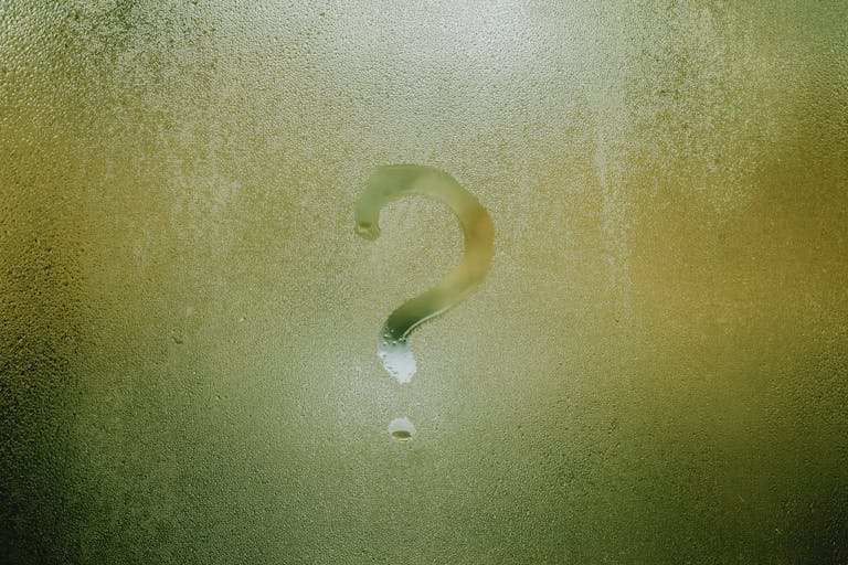 A question mark drawn on foggy glass, evoking curiosity and mystery.