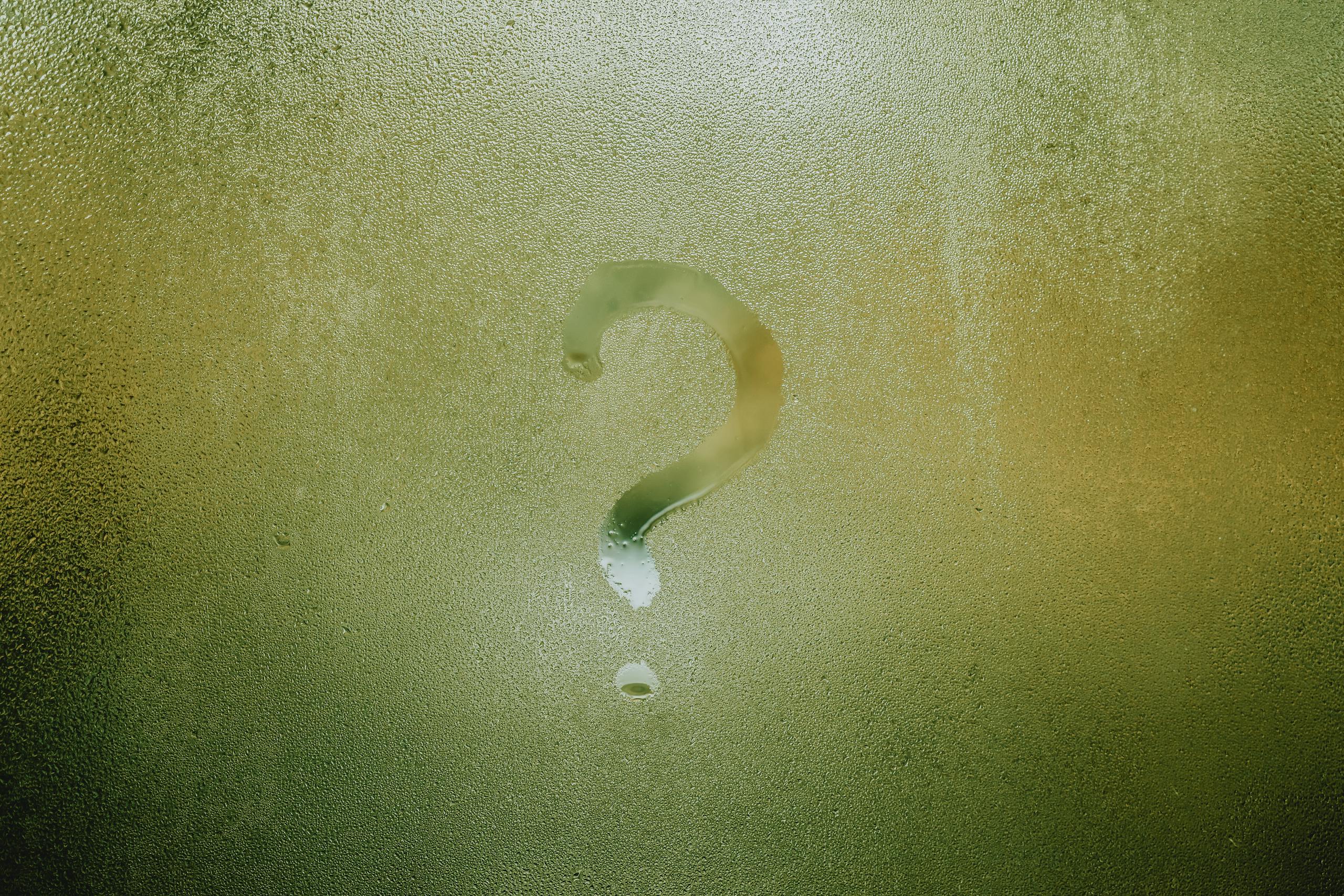 A question mark drawn on foggy glass, evoking curiosity and mystery.